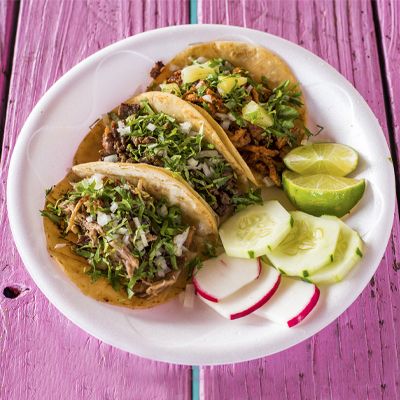 Three street tacos with cilantro, onion and lime